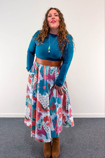 A woman modeling a vintage inspired dress styled with a brown belt and brown suede boots against a plain white wall.