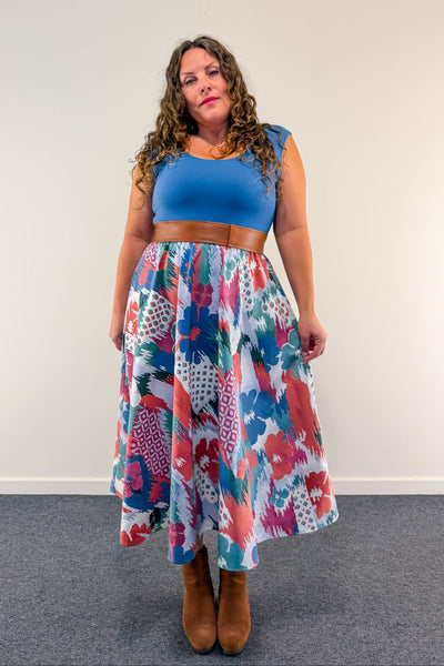 A woman stands in a studio wearing a vintage inspired, midi length dress with full skirt
